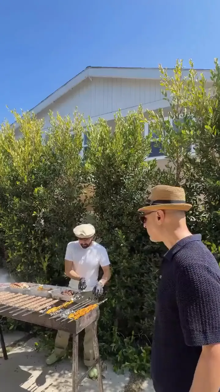 Trays of kebab and rice on a long table under white umbrellas at a private event
