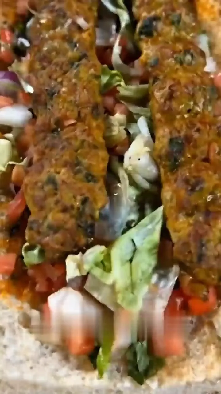 Hands rolling koobideh into warm lavash with salad
