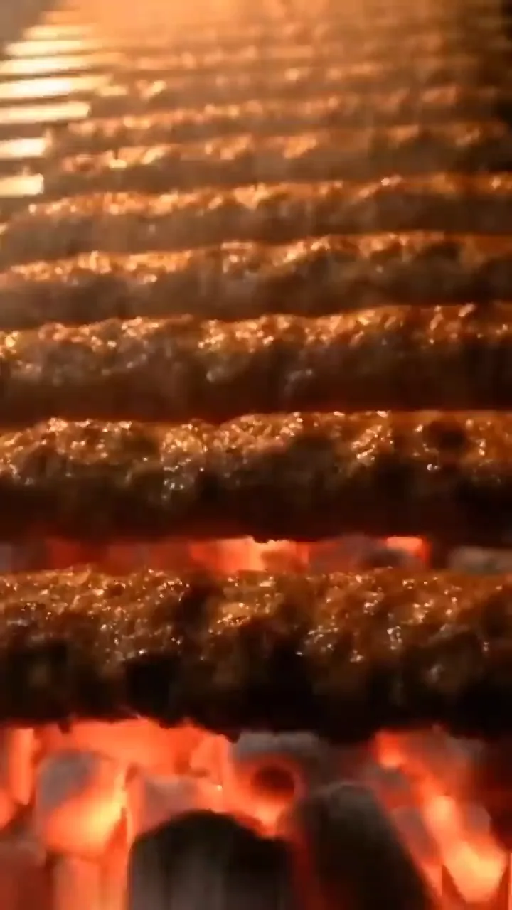 Koobideh skewers on the charcoal grill under string lights, smoke rising