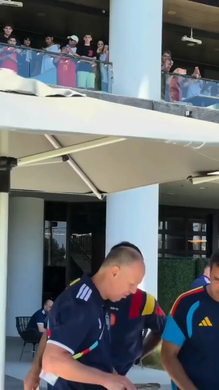 Two members of Spain's delegation in national team training kit serving themselves kebab from foil trays under white umbrellas